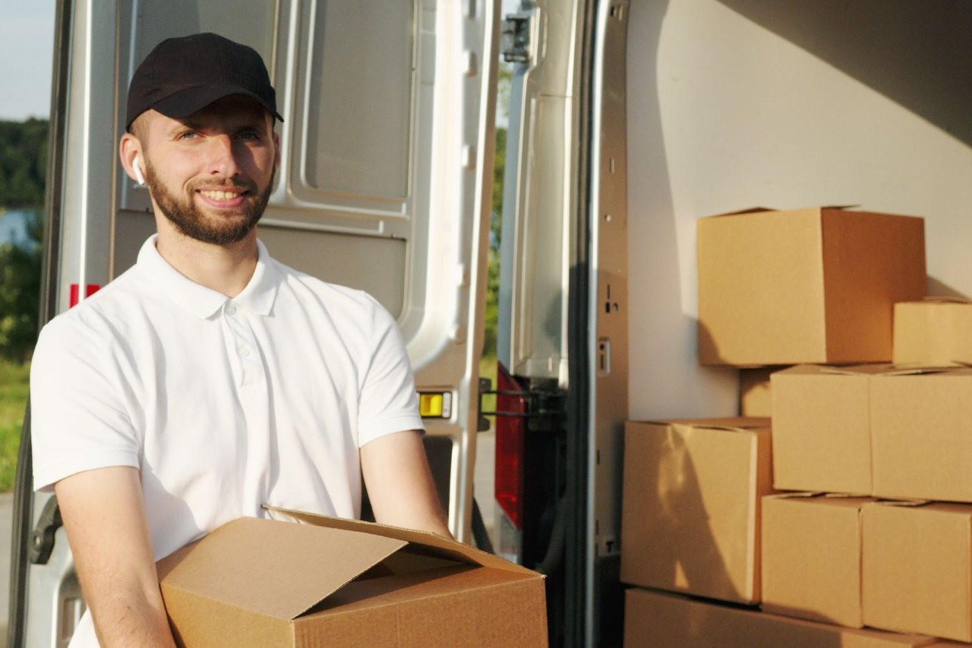 A mover holding a carton at the open side door of a van, boxes stacked behind him.