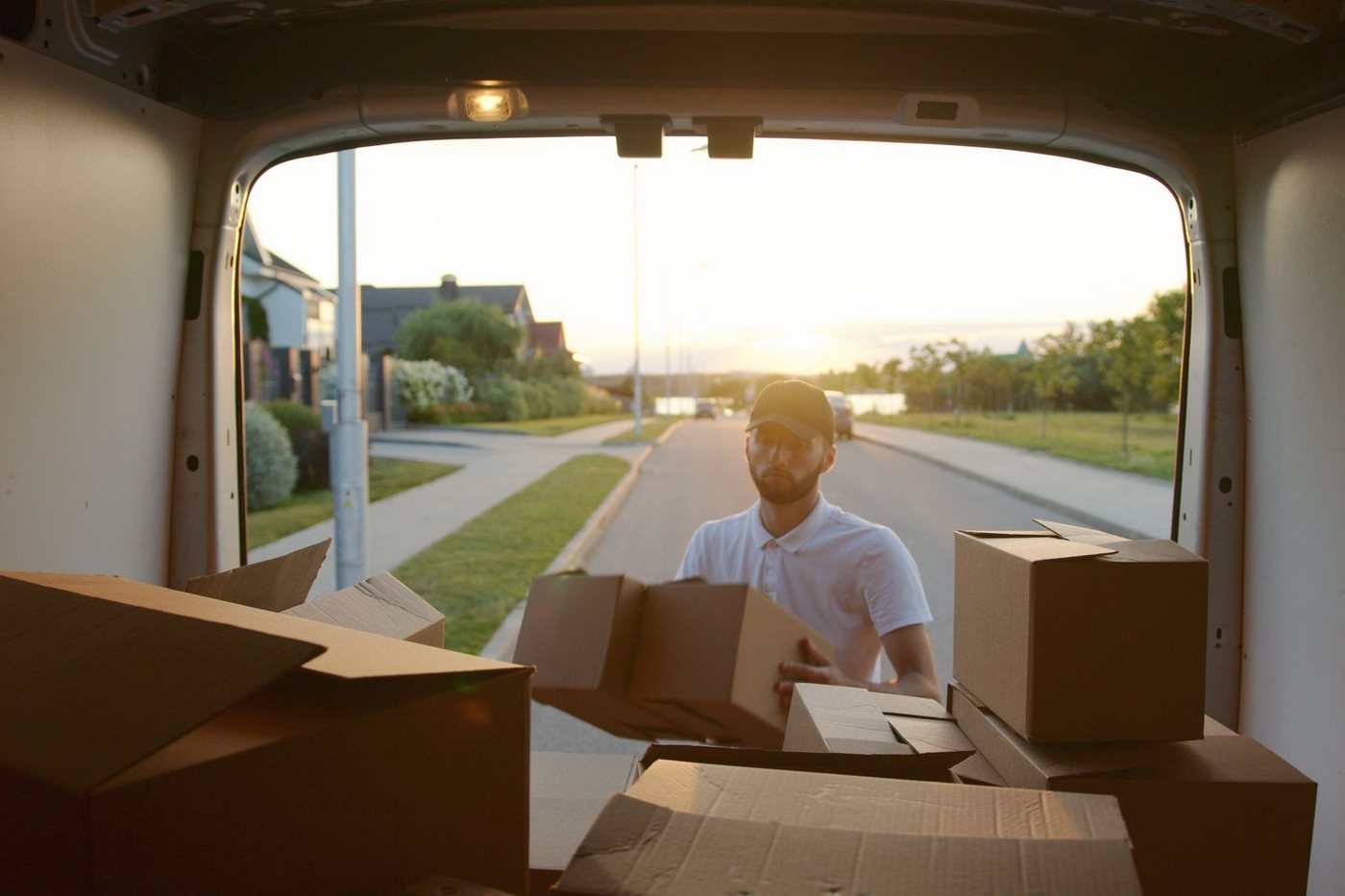 The open rear of a van at sunset as a mover lifts a carton in outside the house.