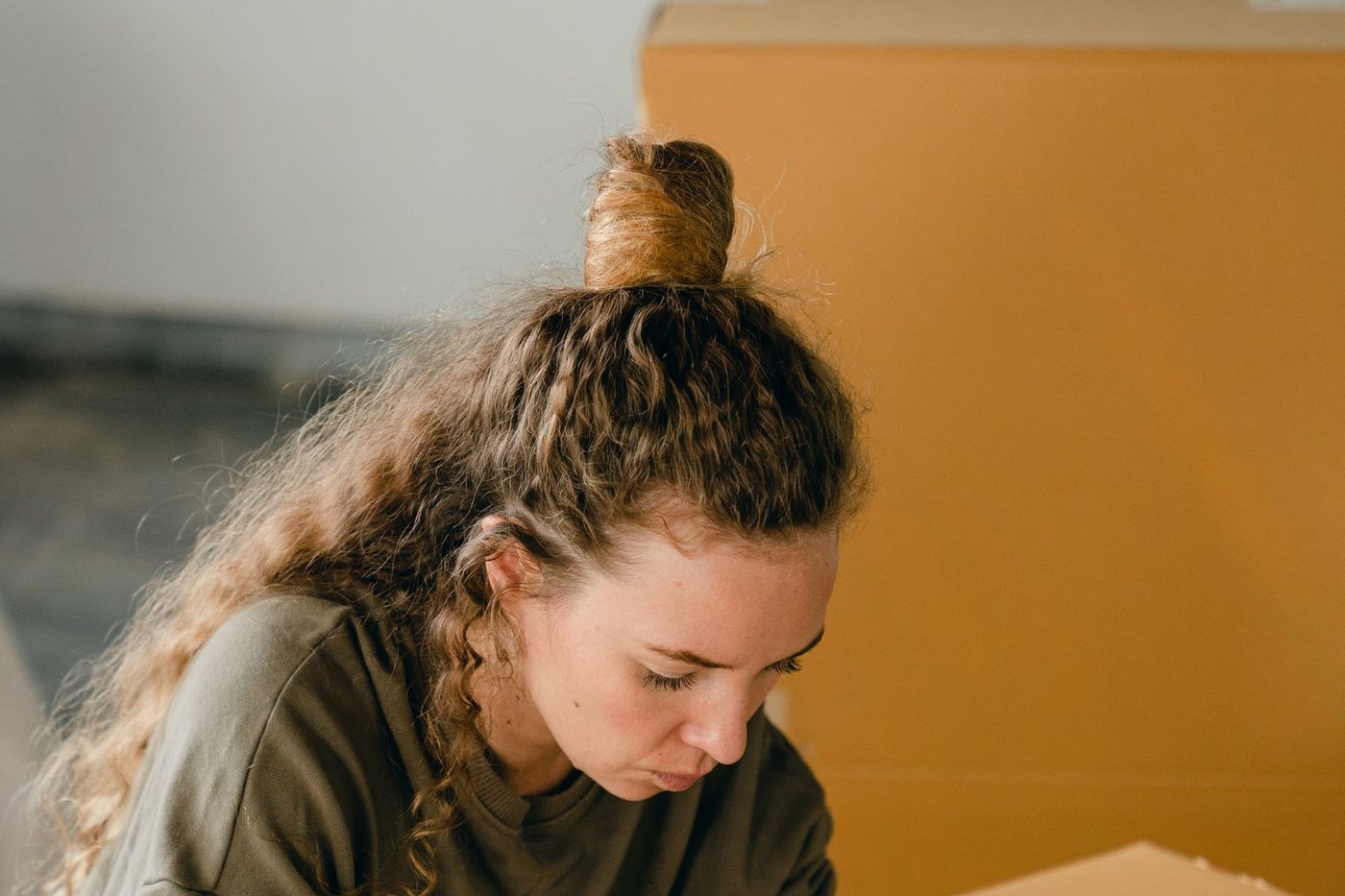 A woman leaning over a carton to write on the lid, packing materials spread around her.