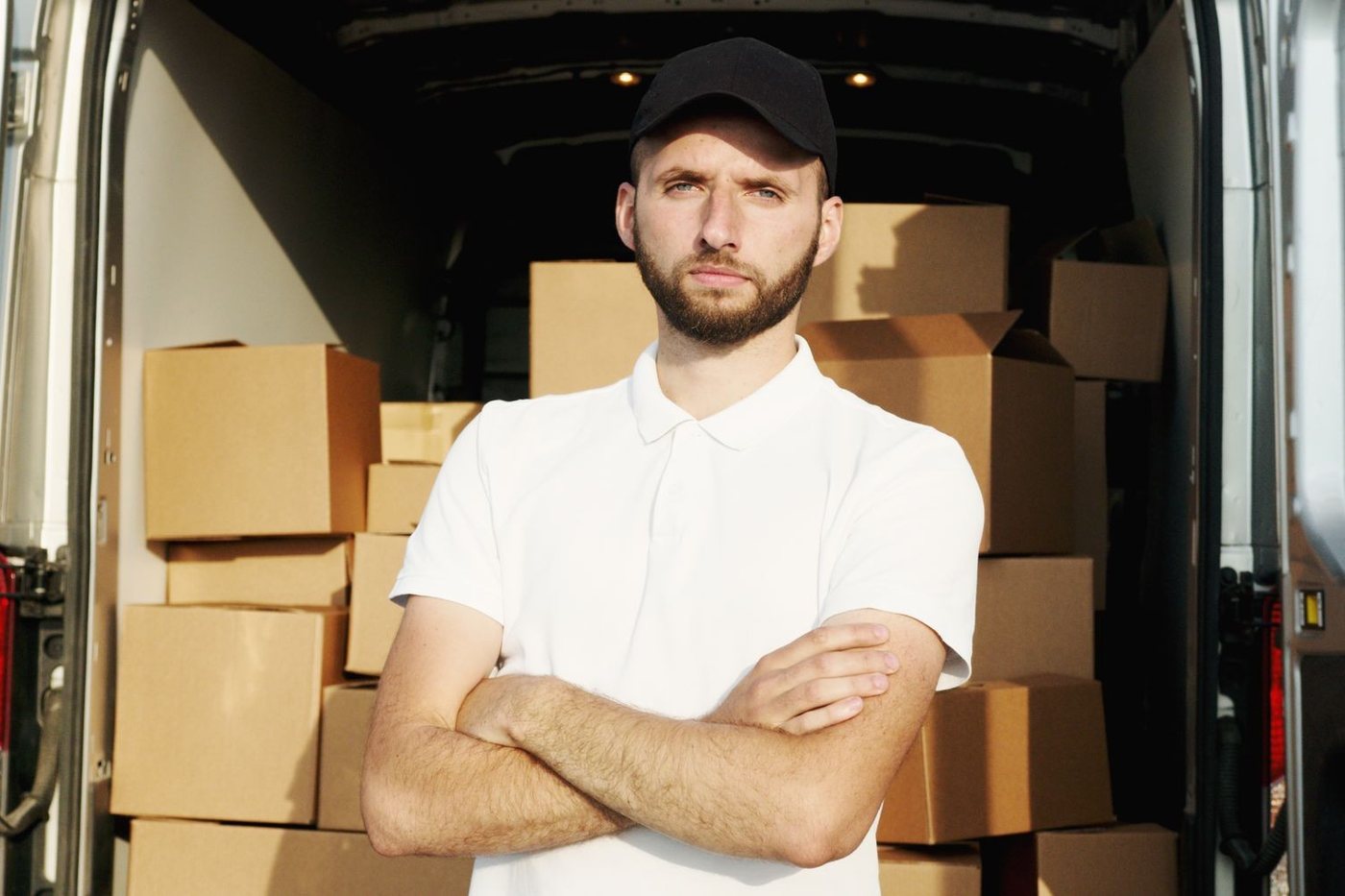 A mover at the rear of a fully loaded van, arms folded, the load squared off behind him.
